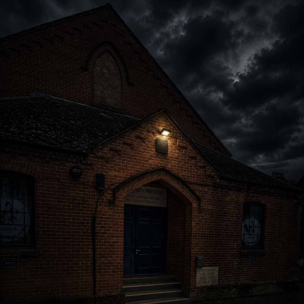 Brick theatre at night with a single warm light above the door and a dark, stormy sky overhead.