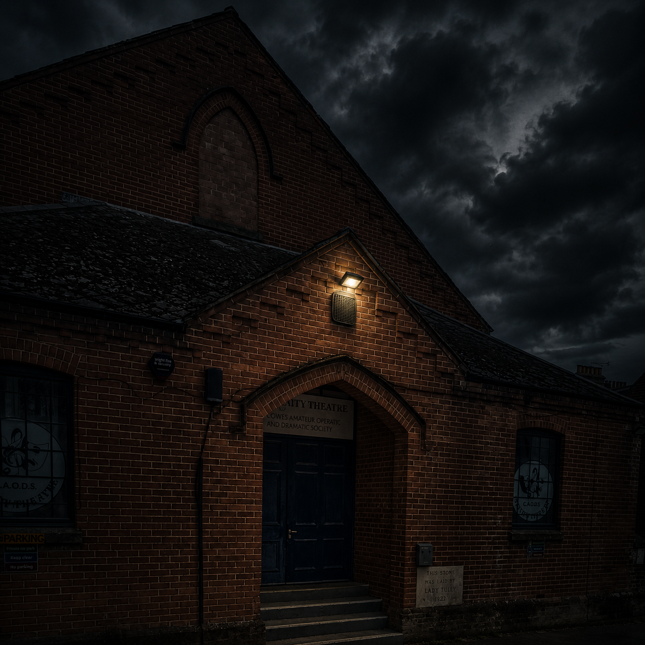 Brick theatre at night with a single warm light above the door and a dark, stormy sky overhead.